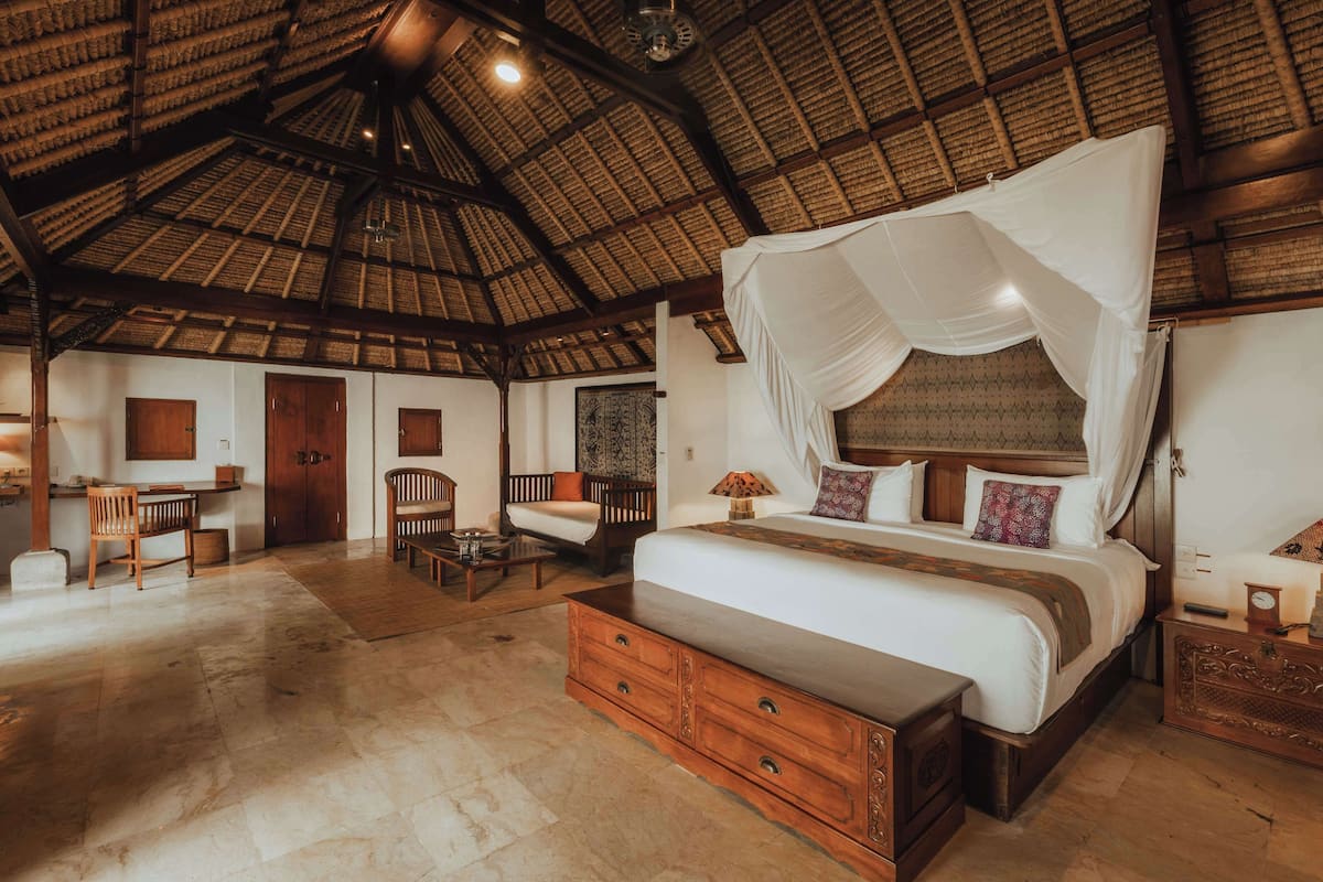 A spacious room with a large bed, wooden furniture, and a high ceiling with a thatched roof.
