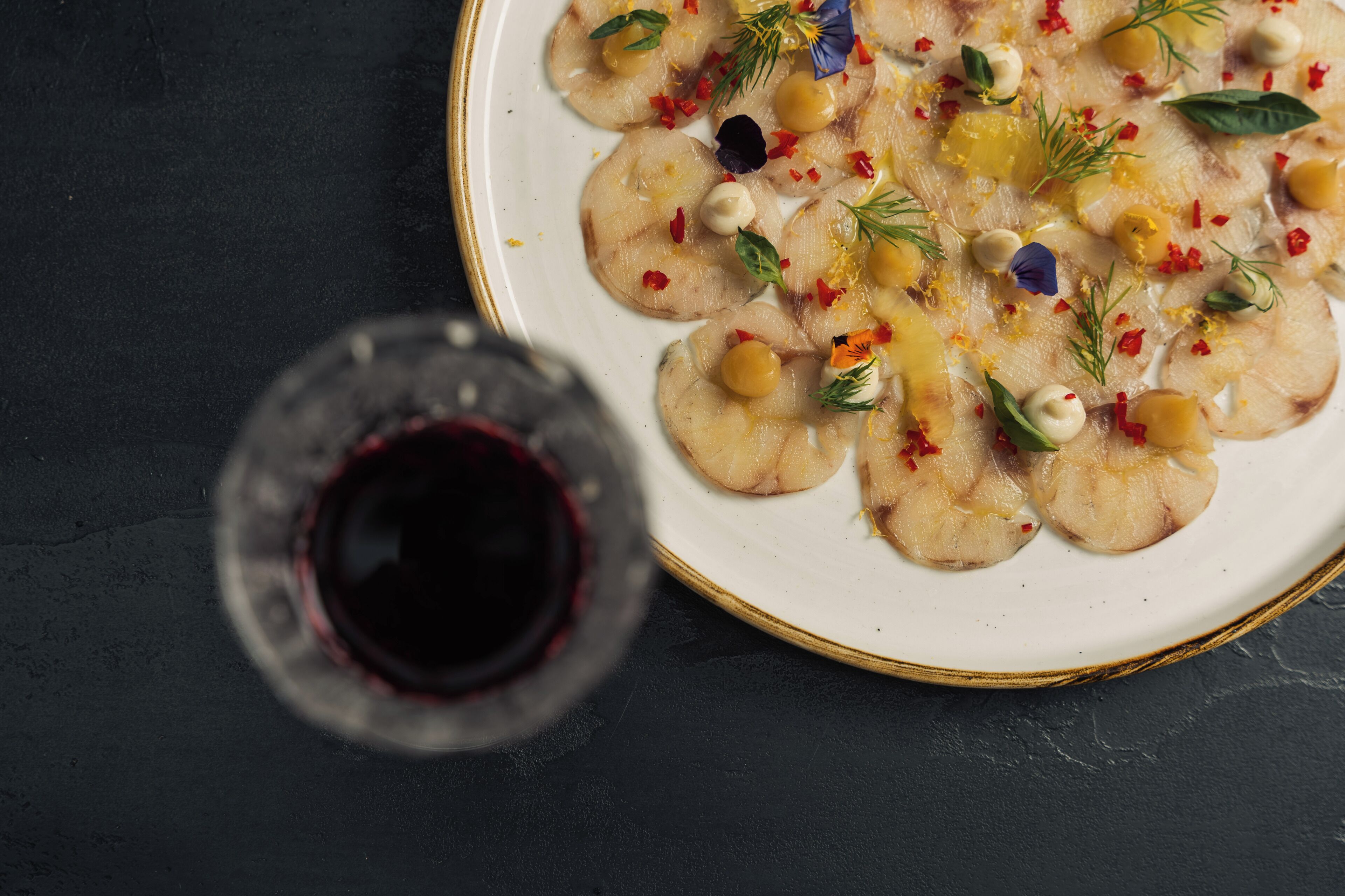 Un plato de comida con diferentes adornos y una copa de vino tinto.