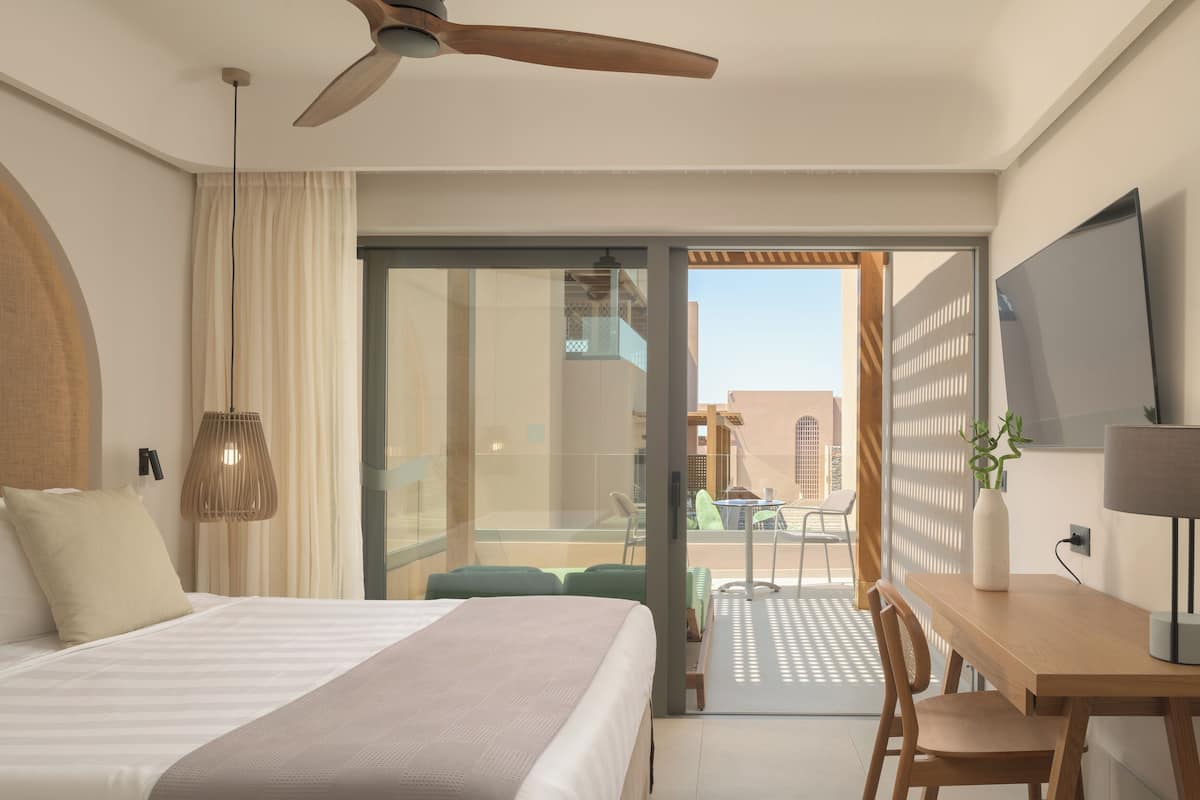 A hotel room with a bed, a desk, a TV, and a balcony with a table and chairs.