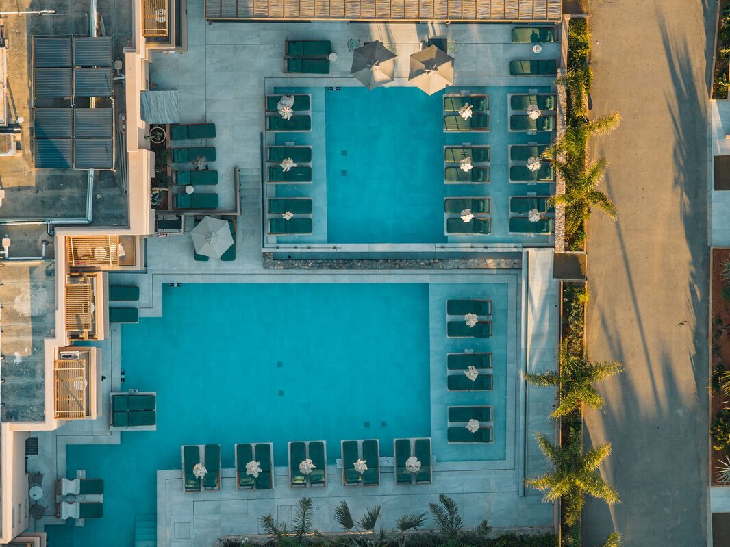 Vue aérienne d’un hôtel doté d’une piscine centrale, de plusieurs espaces de détente et d’un parking.