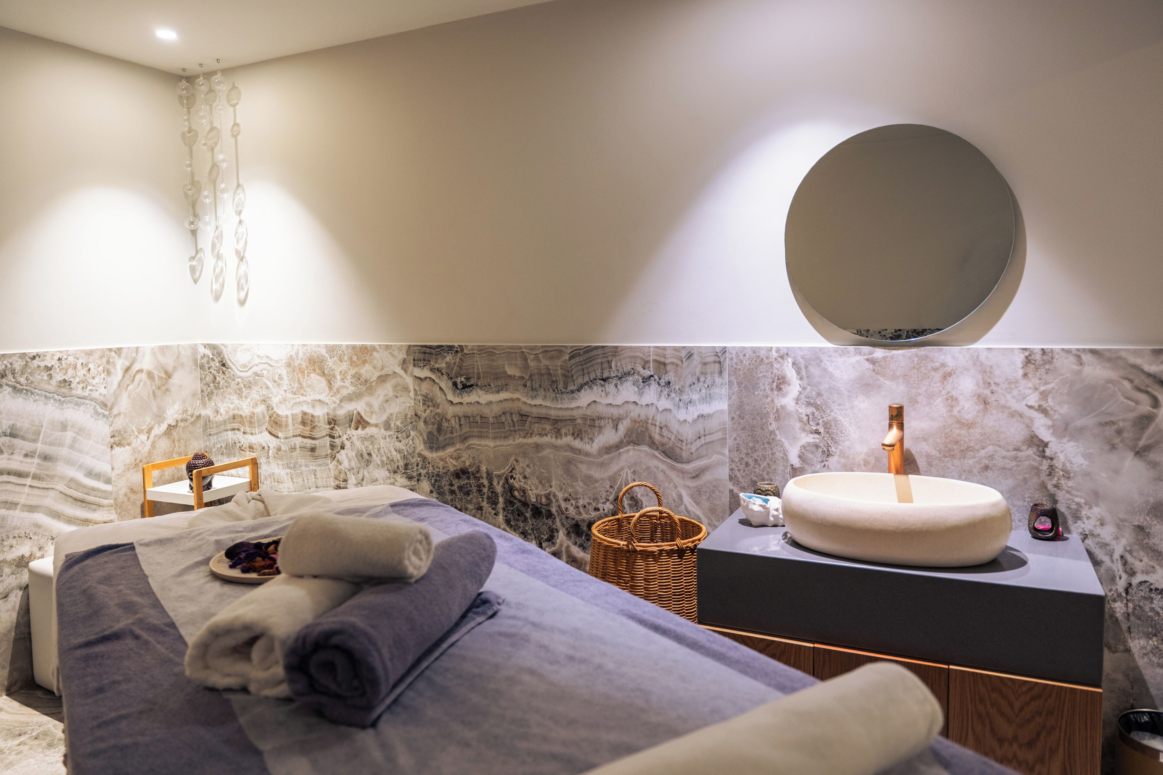A modern bathroom with a marble wall, a round mirror, and a sink with a gold faucet.