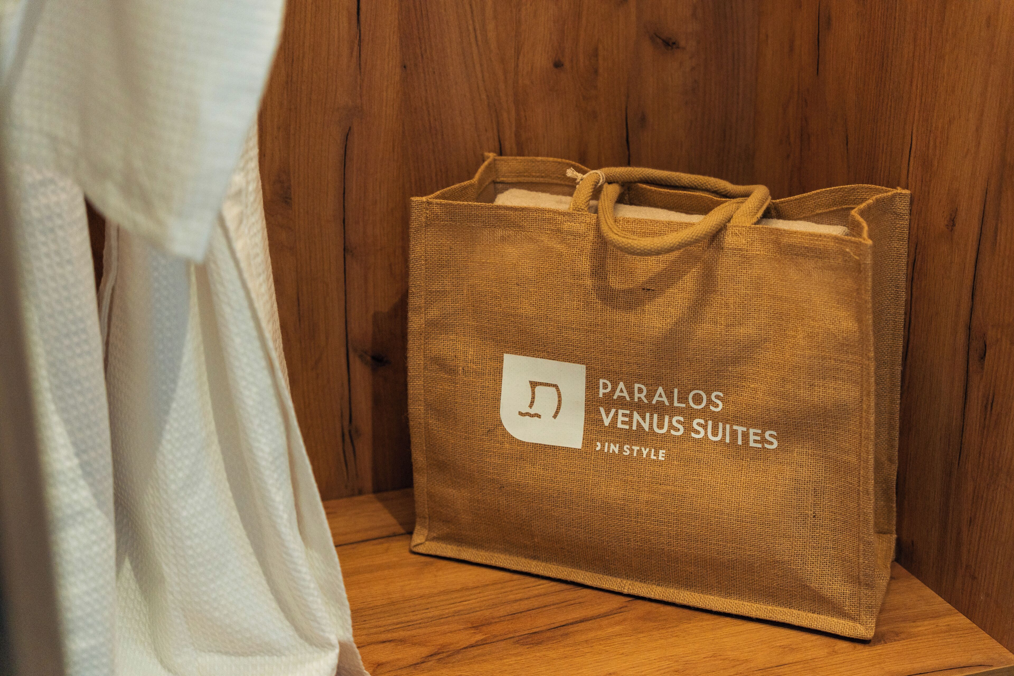 Una bossa de paper marró amb la inscripció 'PARALOS VENUS SUITES' sobre una superfície de fusta.