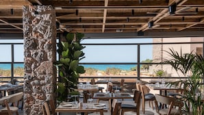 Un área de comedor al aire libre con pilares de piedra, mesas y sillas de madera, con vistas panorámicas al océano.