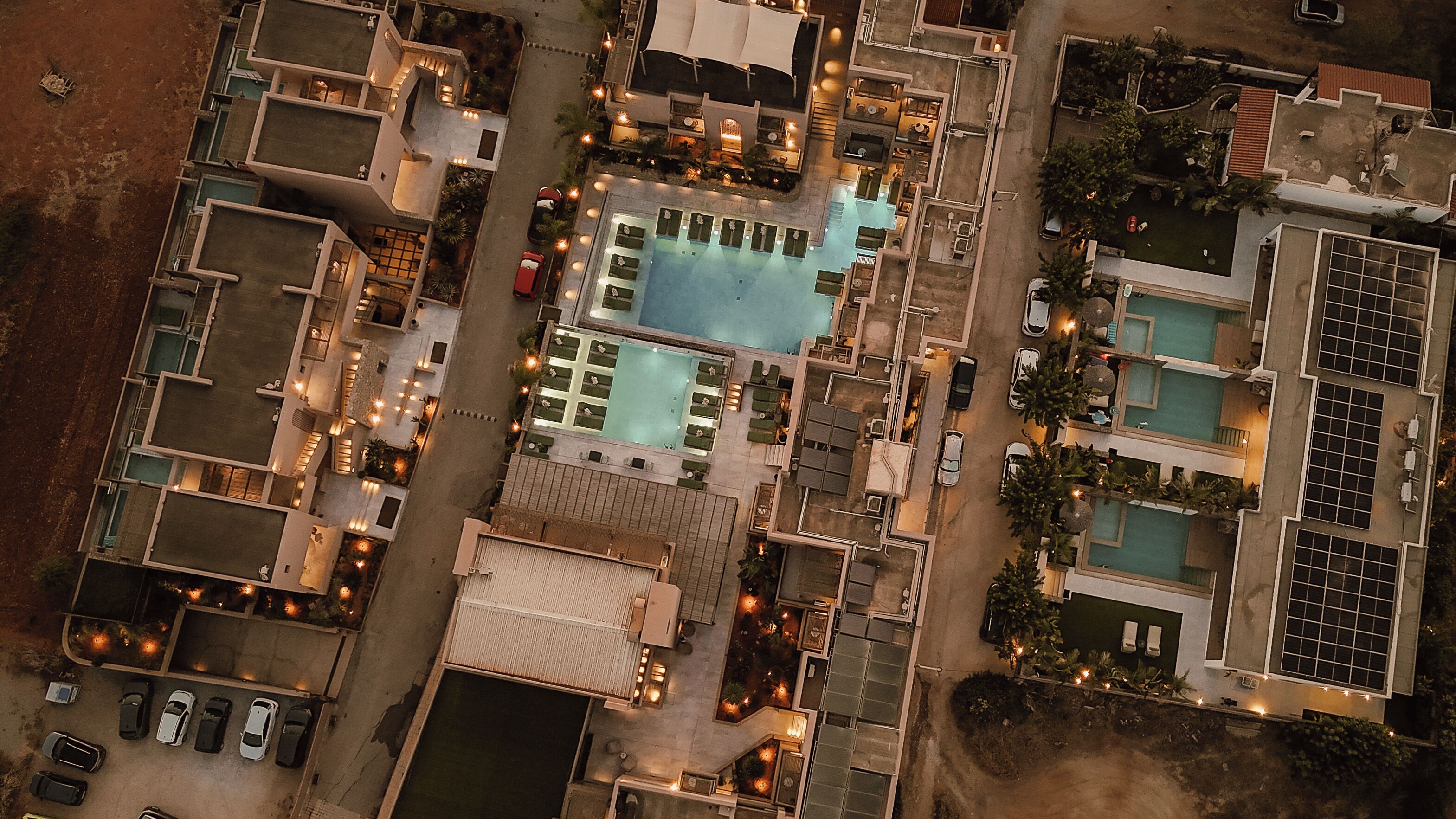 An aerial view of a hotel with multiple swimming pools, a parking area, and a well-lit outdoor space.