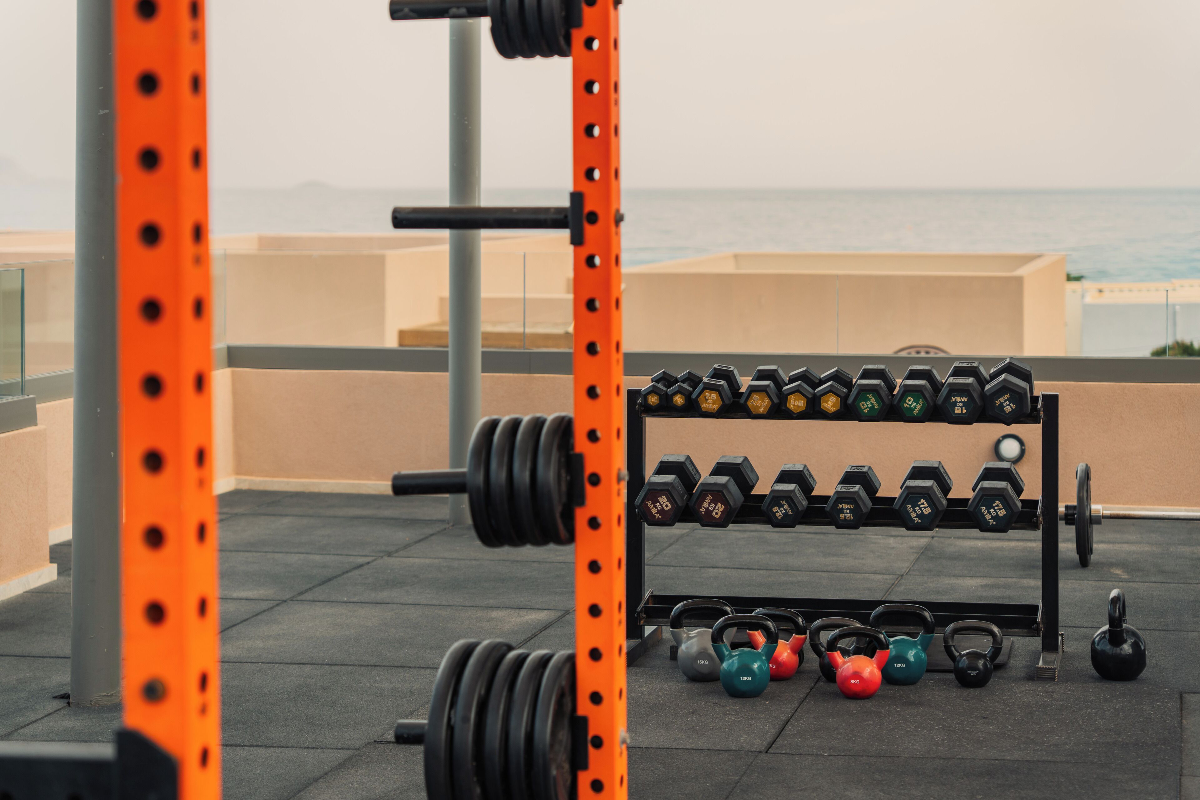 A gym with weightlifting equipment, including dumbbells and kettlebells, on an outdoor platform with a view of the sea.