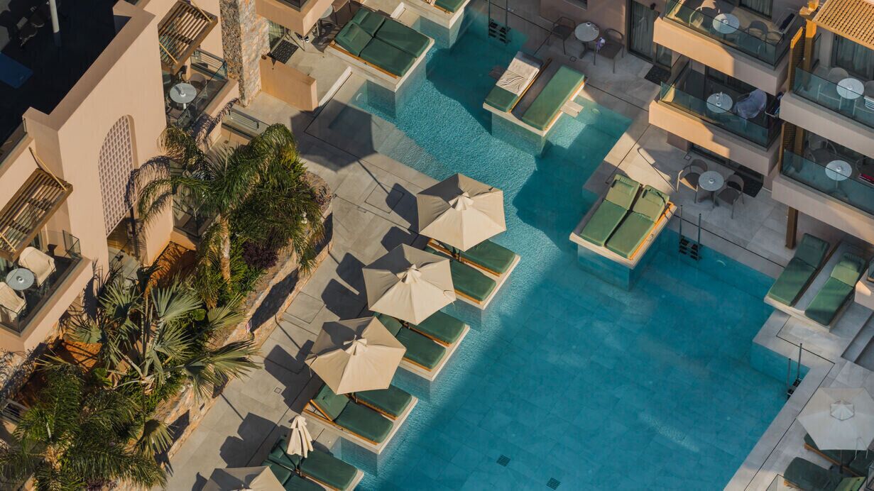 Vue aérienne d’un hôtel doté de plusieurs piscines, de chaises longues et de palmiers.