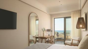 Een hotelkamer met een bed, een bureau, een stoel en een grote spiegel. Er is uitzicht op het strand door het raam.