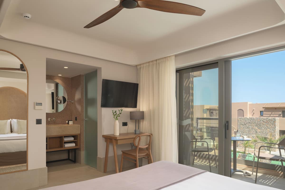 A hotel room with a bed, desk, chair, TV, and a balcony with outdoor seating.