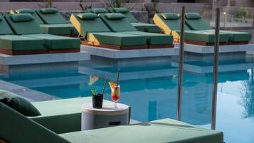 Zona de piscina con sillas reclinables verdes y una bebida sobre una mesita.