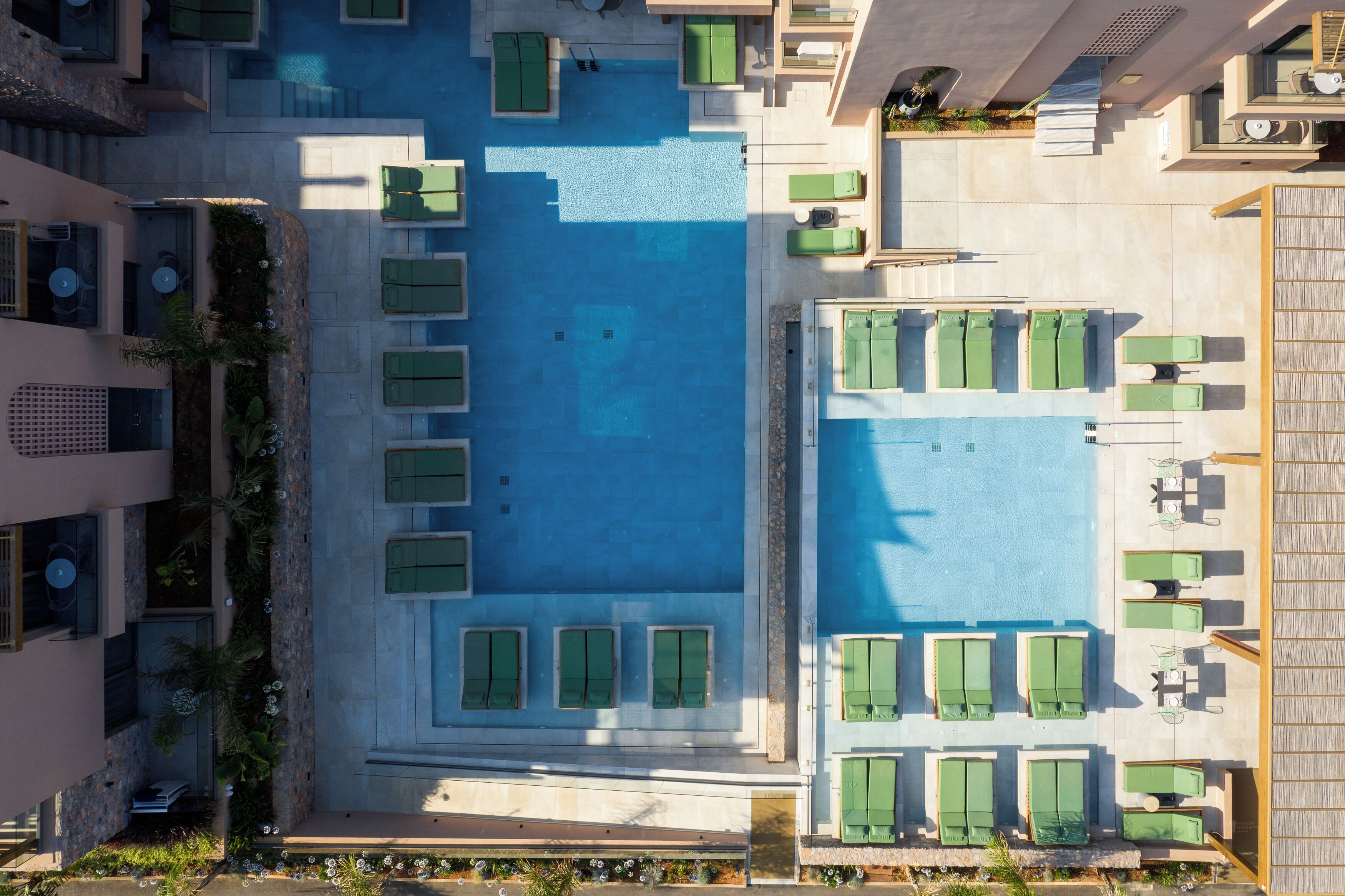 Vue aérienne d’un hôtel doté d’une piscine centrale, entourée d’espaces de détente aménagés avec des meubles verts.