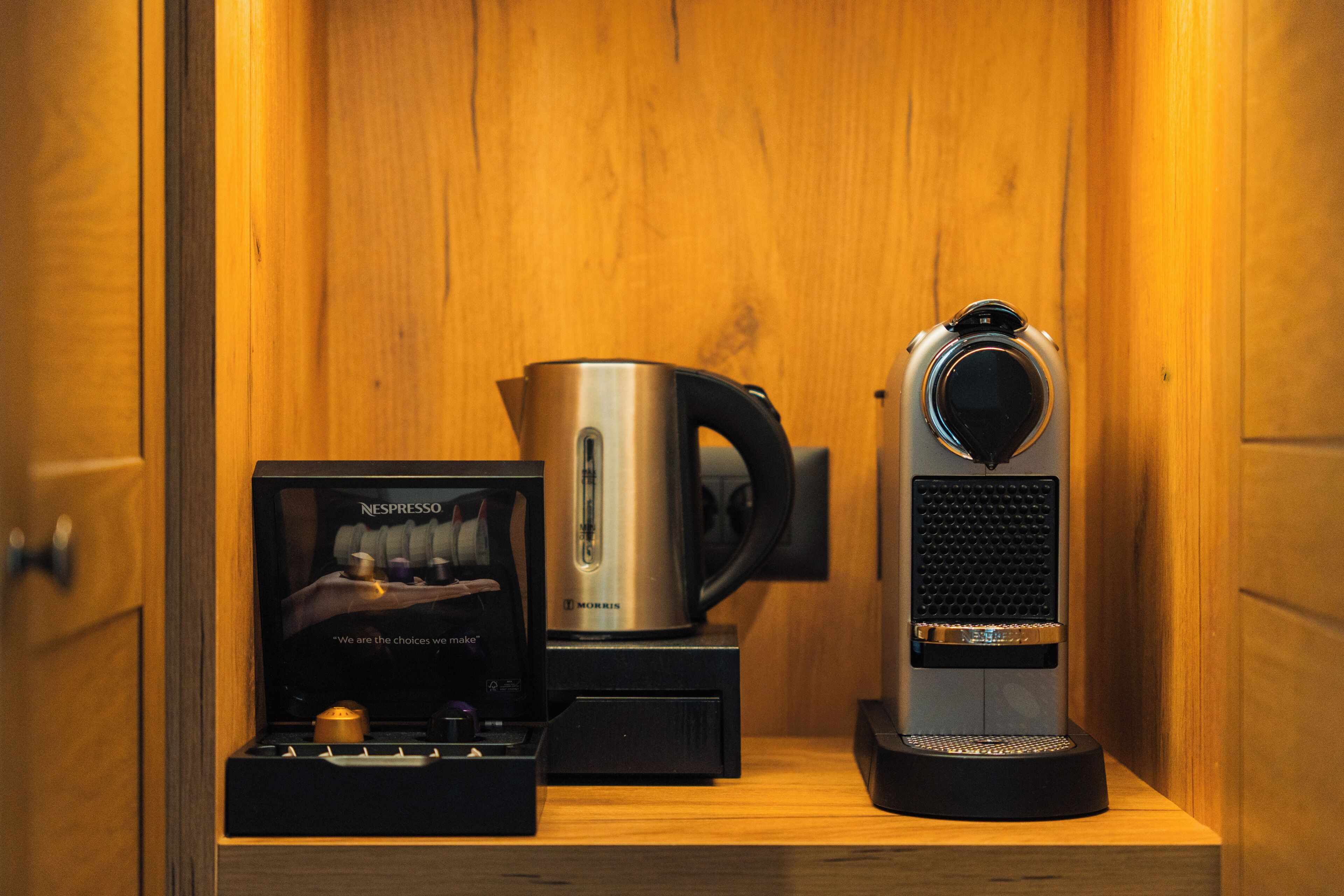 Eine Kaffeemaschine, ein Wasserkocher und eine Schachtel mit einer Kaffeemaschine auf einem Holzregal.