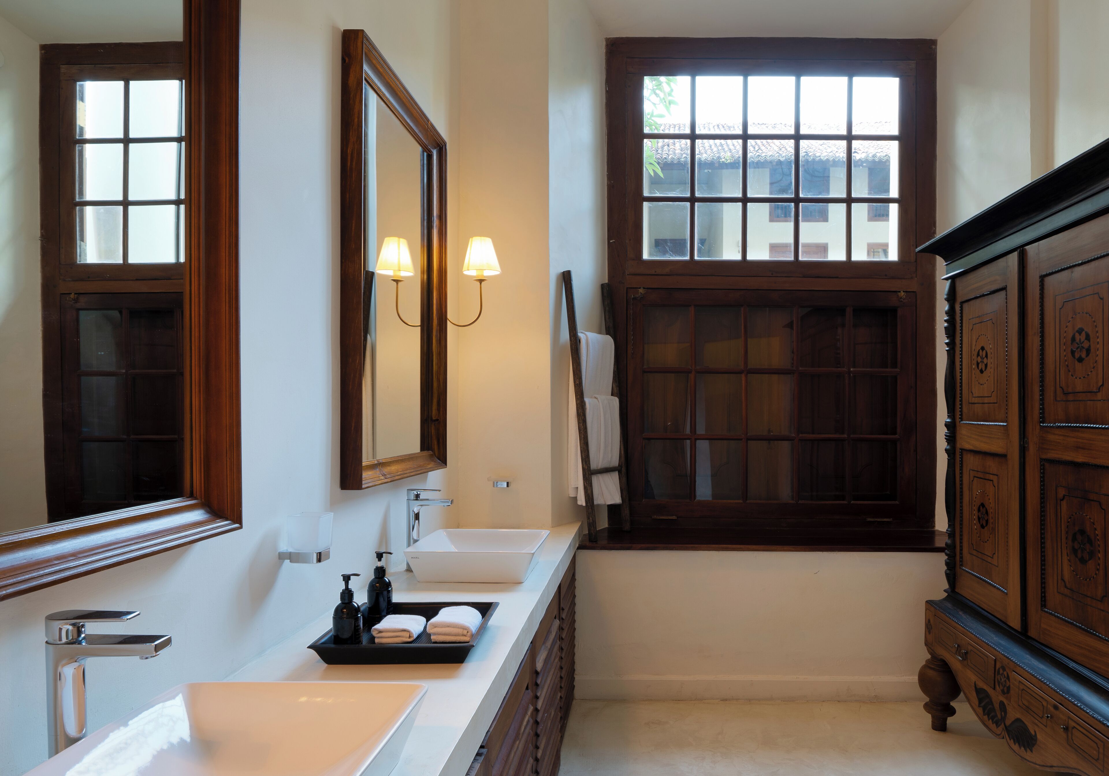 A bathroom with a large mirror, a sink, a window with a view, and a wooden cabinet.