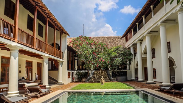 A pool area with lounge chairs, a clear pool, and a building with columns and a tiled roof. - Galle Fort Hotel (Galle)