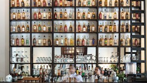 A bar with multiple shelves of liquor bottles, bar stools, and a bartender. - Galle Fort Hotel (Galle)