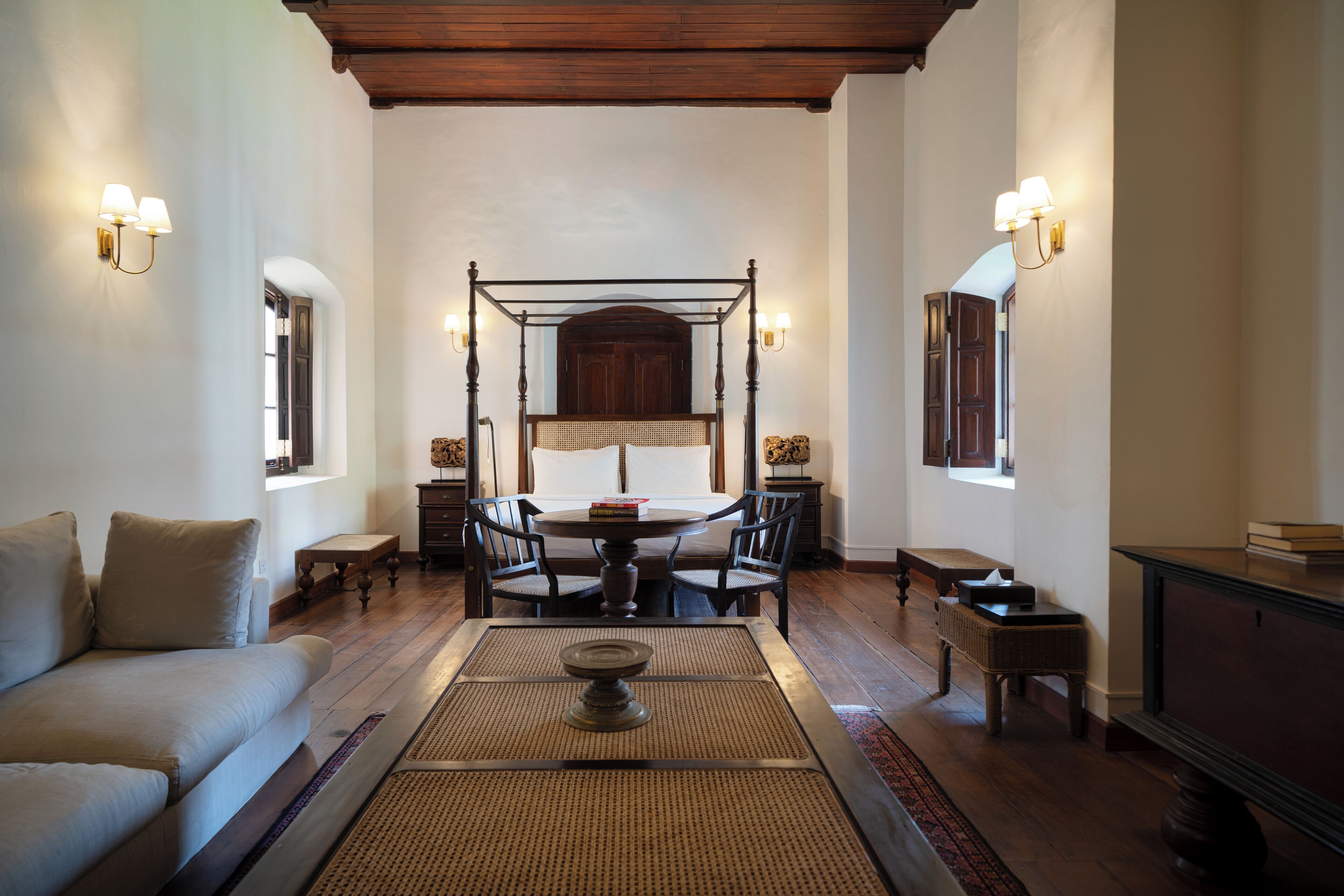 A room with a four-poster bed, a dining table with chairs, a sofa, and a television.