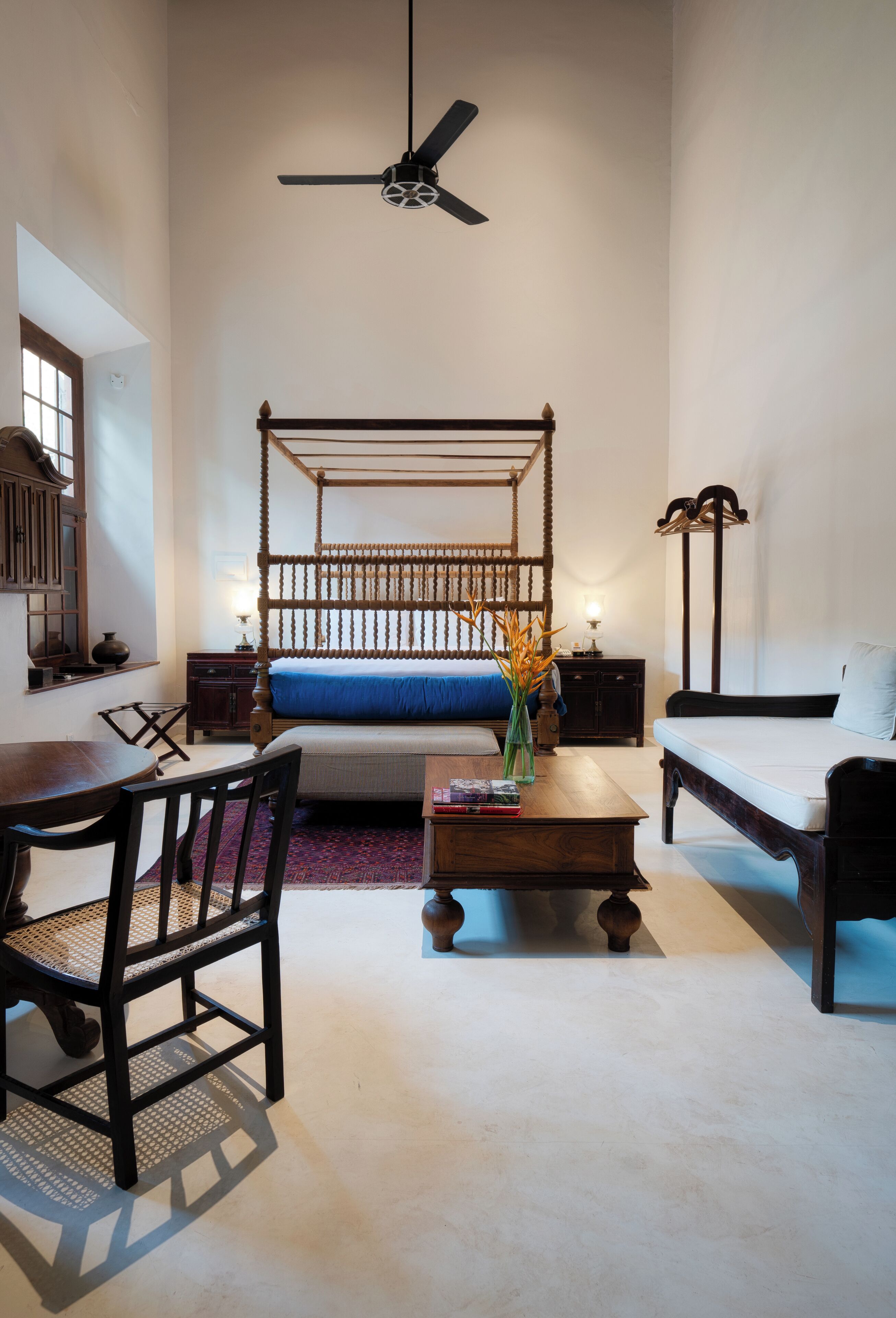 A bedroom with a four-poster bed, a desk, a chair, a sofa, and a ceiling fan.