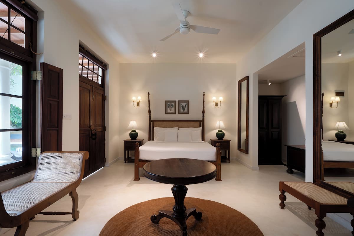 Ett sovrum med en säng, två sängbord med lampor, ett runt bord och en bänk.