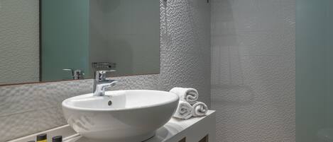 A bathroom with a white sink, mirror, and towel rack. There are four bottles of Honey shower gel on the counter.