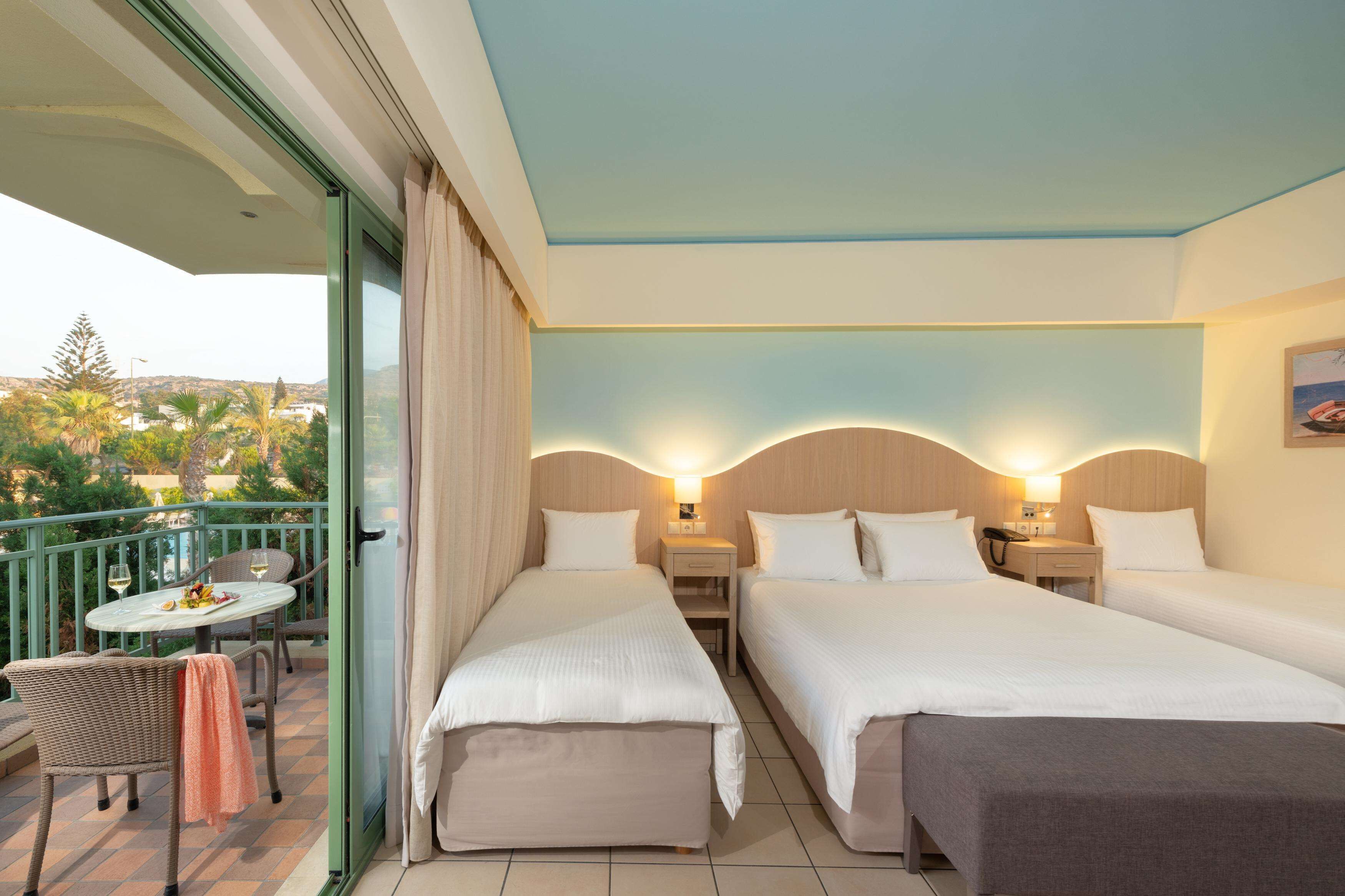 Habitación de hotel con dos camas, un balcón con mesa y sillas, y vistas a la ciudad.