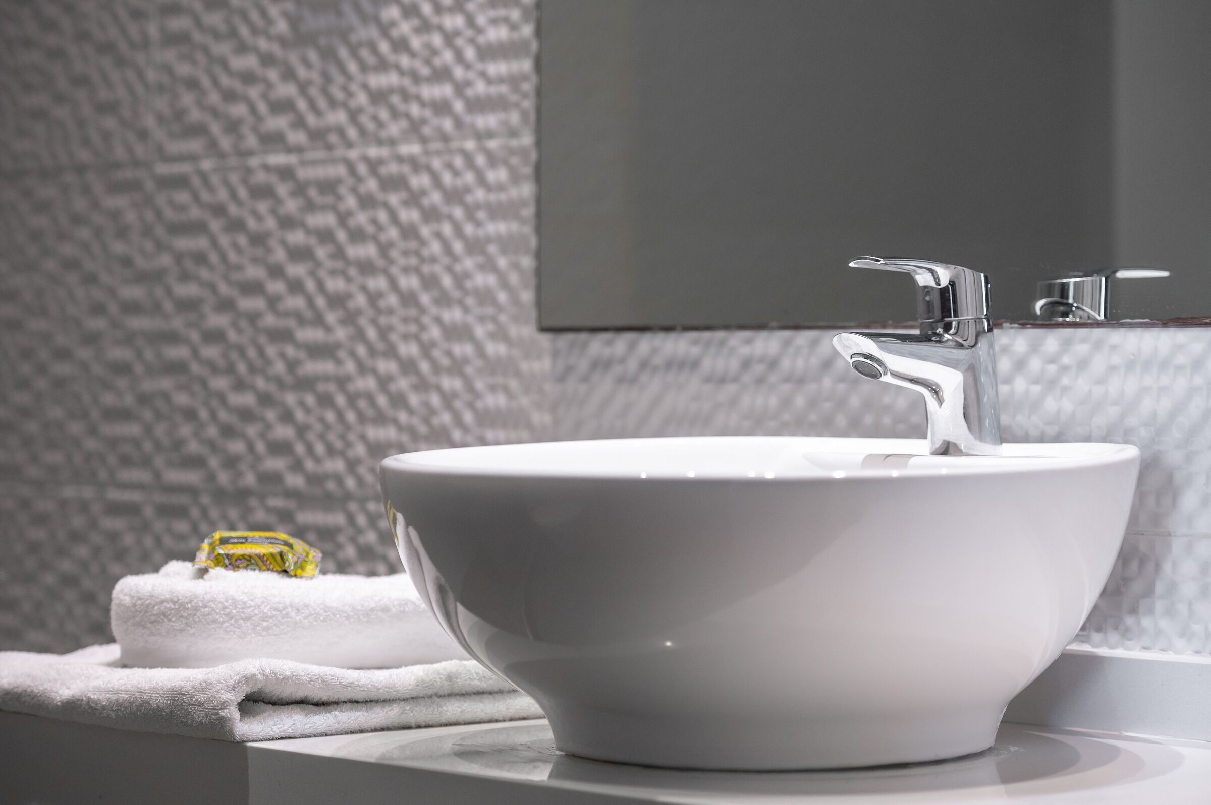 Un lavamanos de cerámica blanca con un grifo moderno, una toalla y un espejo en un baño con pared texturizada.