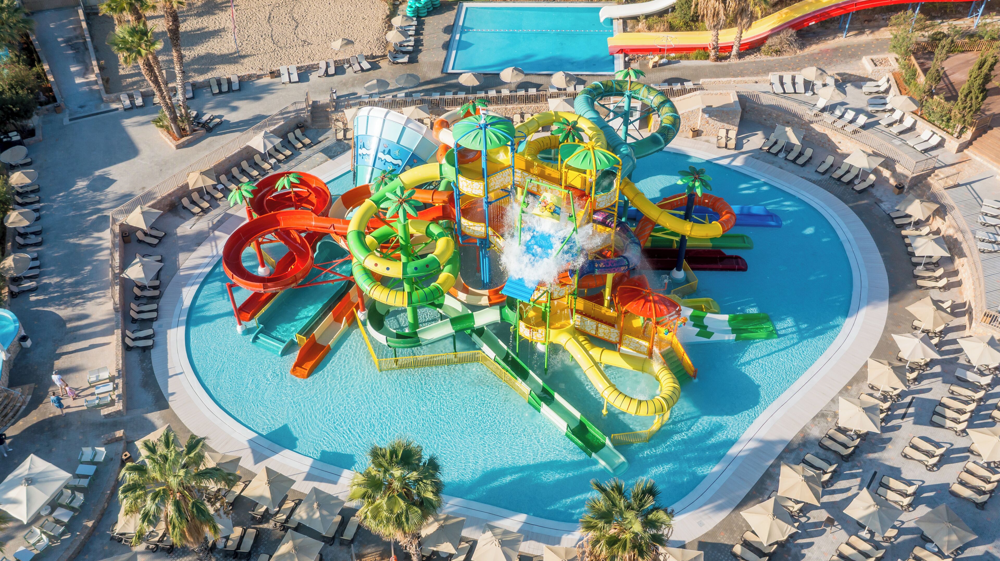 Een waterpark met meerdere glijbanen en zwembaden, omringd door ligbedden en parasols.