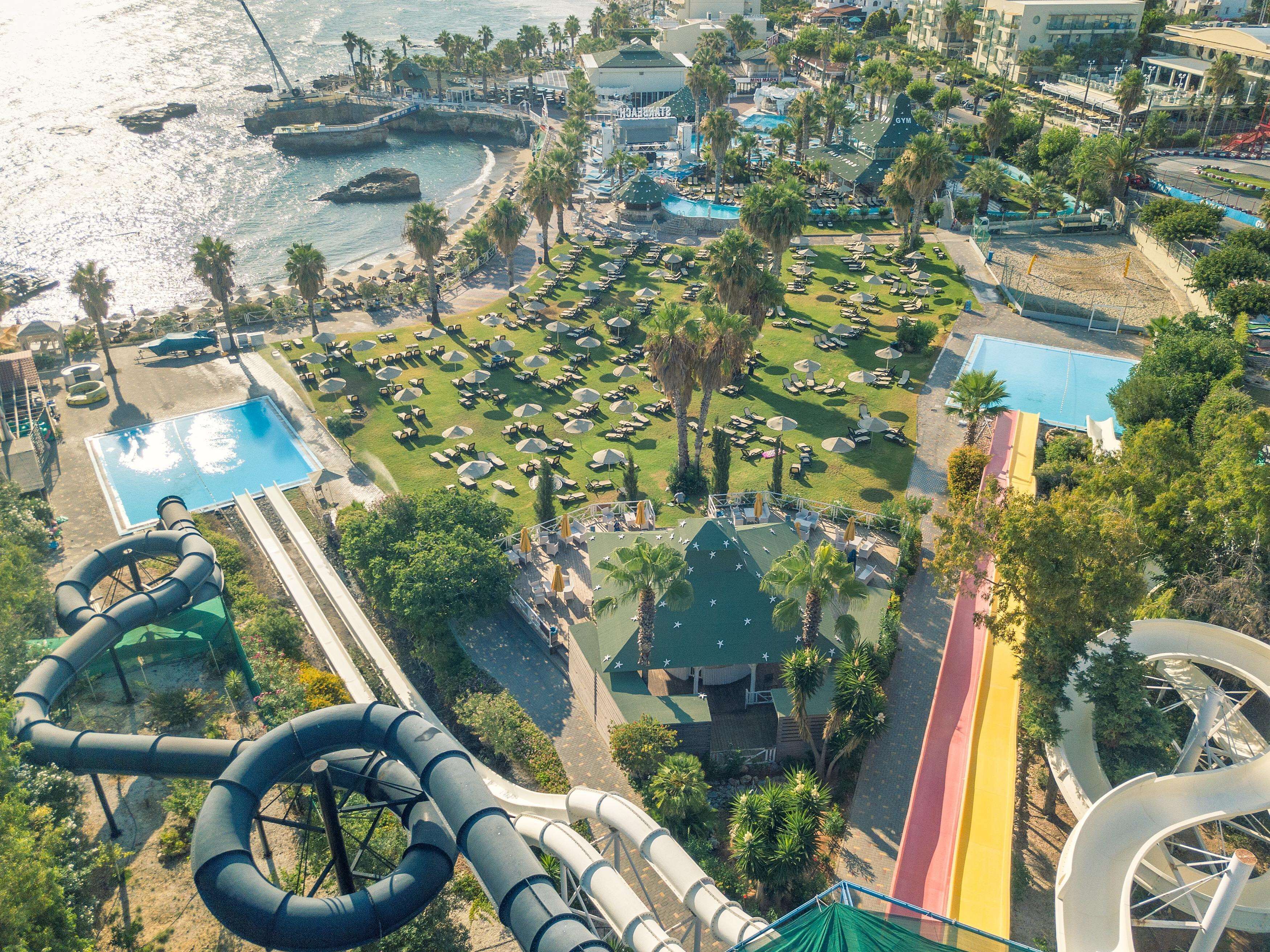 An aerial view of a resort with multiple pools, a water slide, and a beach area with sun loungers.