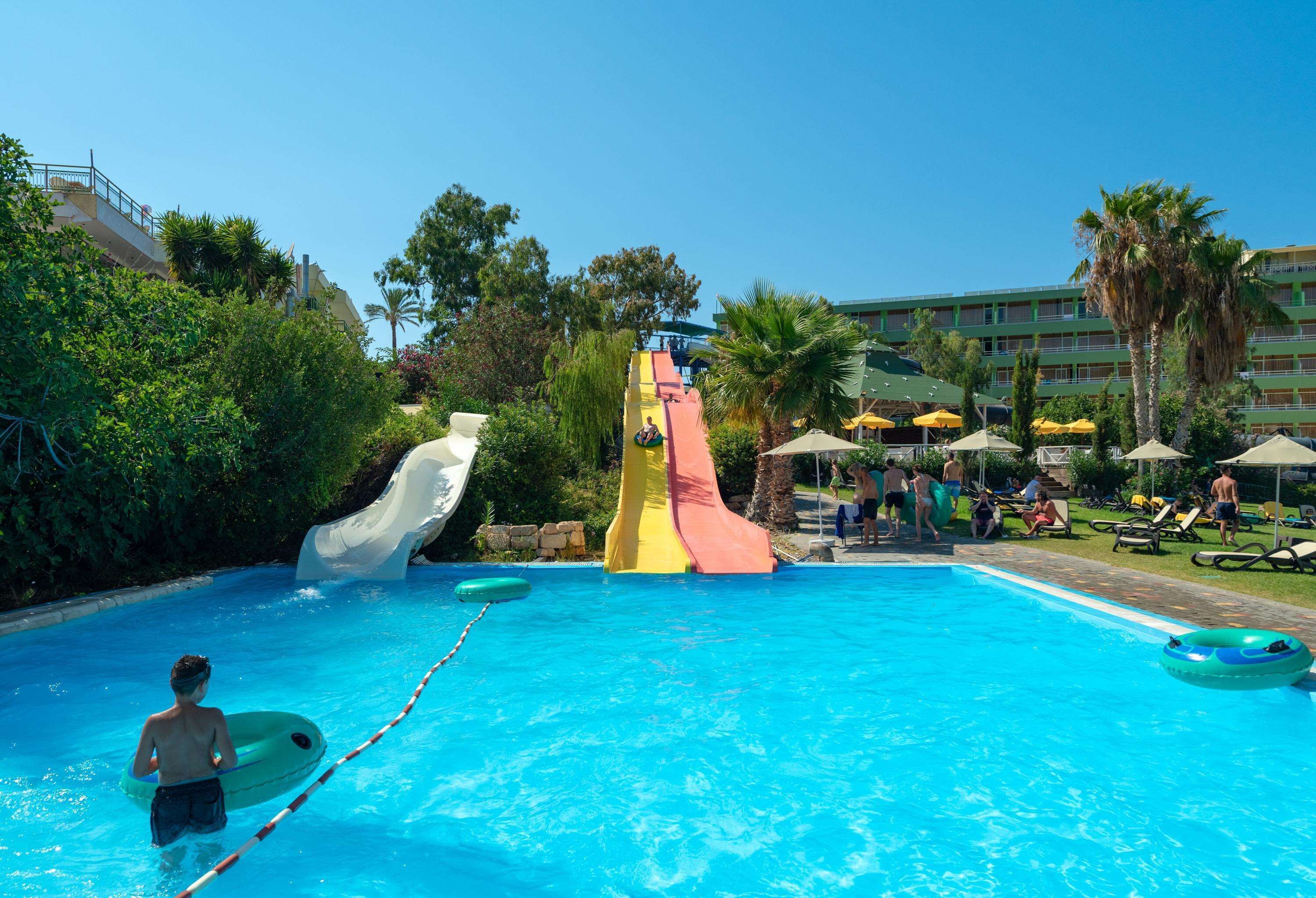 Una piscina con tobogán de agua, sillas de descanso y sombrillas.