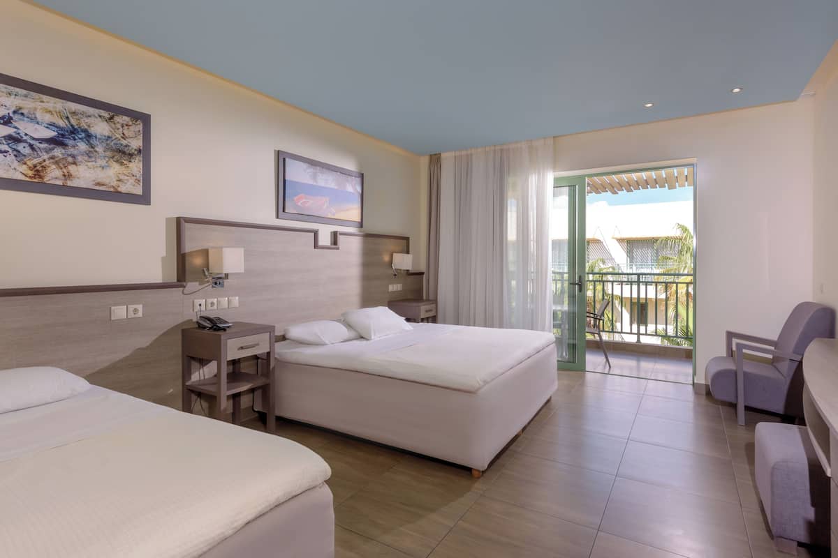 A hotel room with two beds, a desk, a chair, and a balcony with a view.