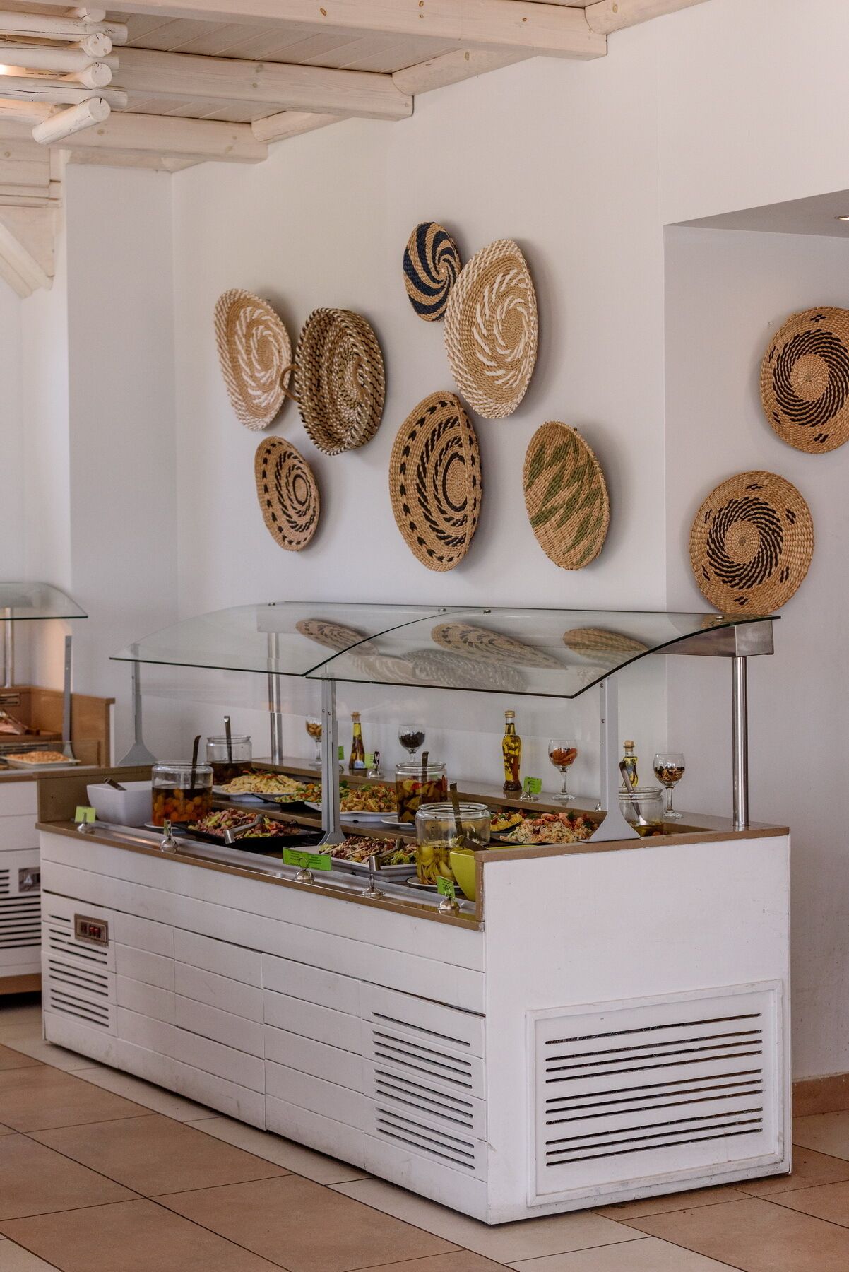 A buffet setup with a glass display case, various food items, and woven placemats on the wall.