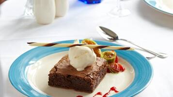 A dessert plate with a brownie and ice cream, accompanied by a glass of red wine and a blue glass.