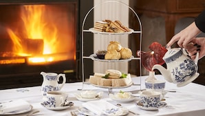 Un présentoir à trois niveaux avec des sandwichs et des scones, une carafe de thé et une théière, le tout posé sur une table recouverte d’une nappe blanche.