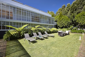 Un bâtiment moderne doté de grandes fenêtres, d’une pelouse bien entretenue et d’un espace extérieur aménagé pour s’asseoir.