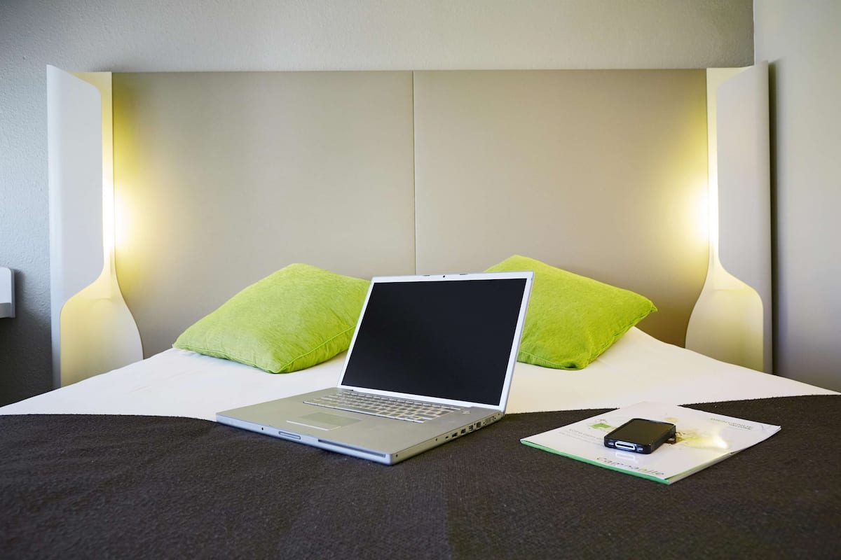 Un lit bien fait, sur lequel on peut voir un ordinateur portable, un téléphone intelligent et un petit livre.