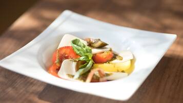 A square white plate with a salad consisting of tomatoes, basil, and mozzarella on a wooden table.