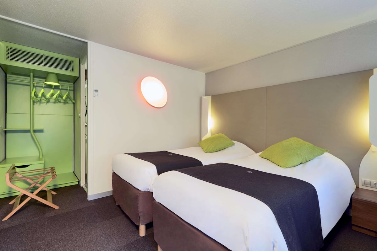 Une chambre d’hôtel avec deux lits, un meuble mural vert et une chaise en bois.