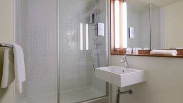 Un baño moderno con ducha acristalada, un lavabo blanco y un espejo encima.