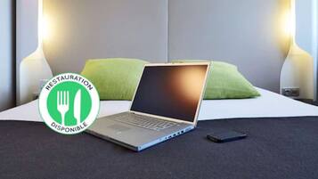 Quarto de hotel com uma cama, um laptop e um smartphone no chão.