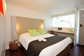 Une chambre à coucher bien rangée, avec un lit, une table de chevet, une lampe et une fenêtre.