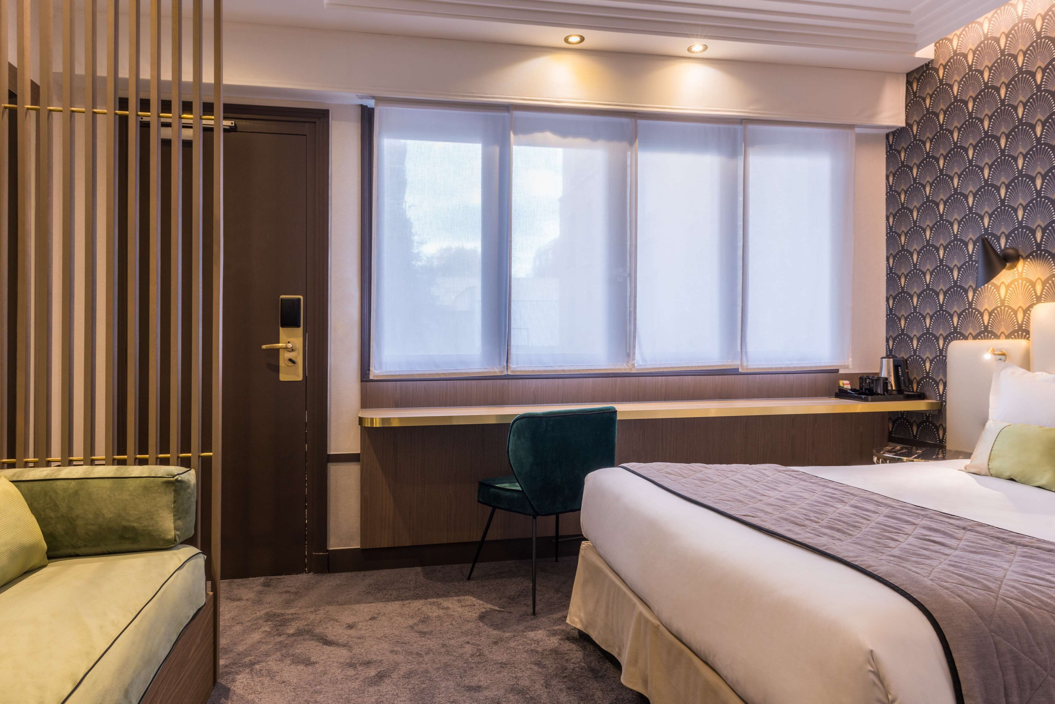 A hotel room with a bed, a desk, a chair, and a window with blinds.