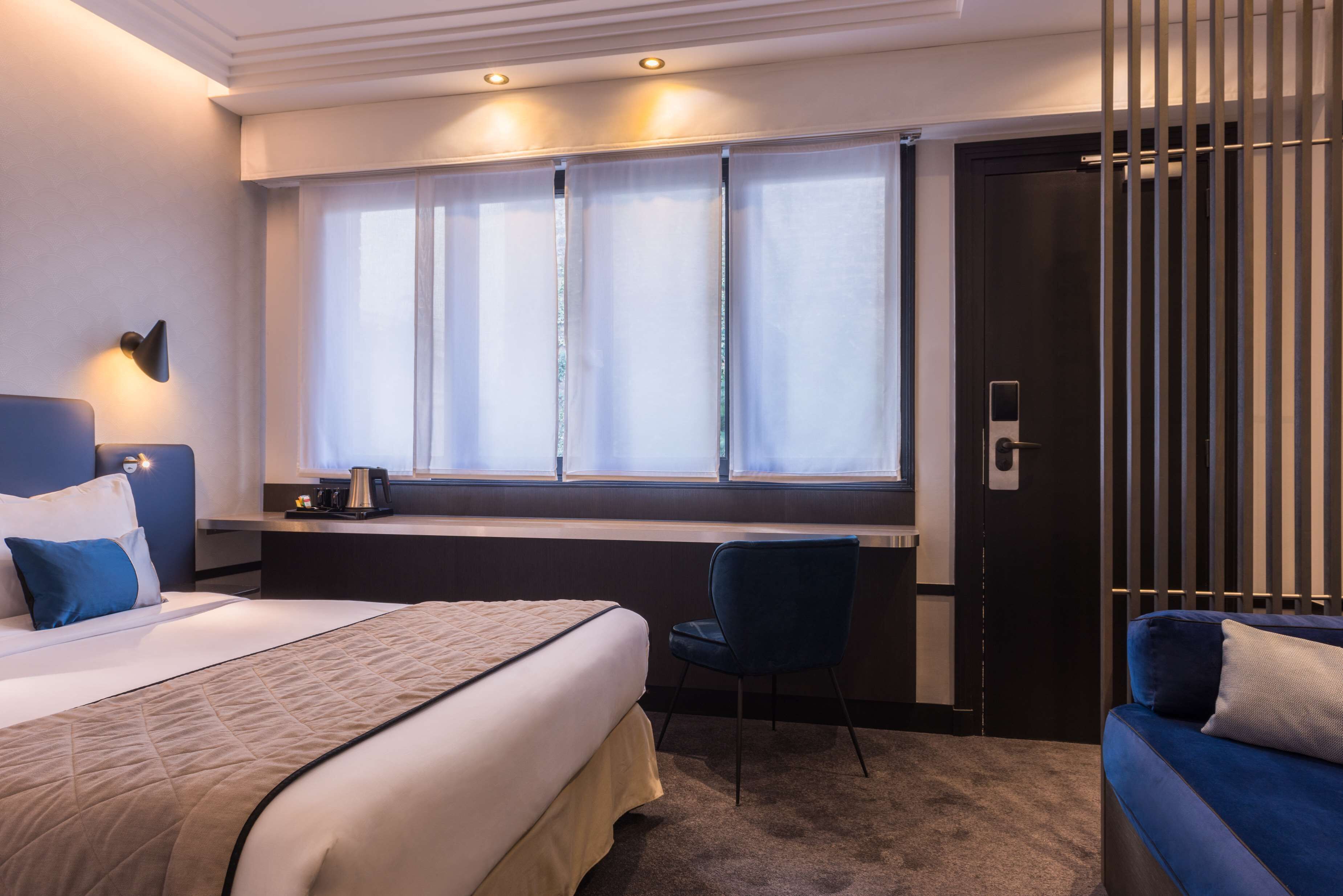 Une chambre d’hôtel avec un lit, un bureau, une chaise et une fenêtre avec des rideaux.