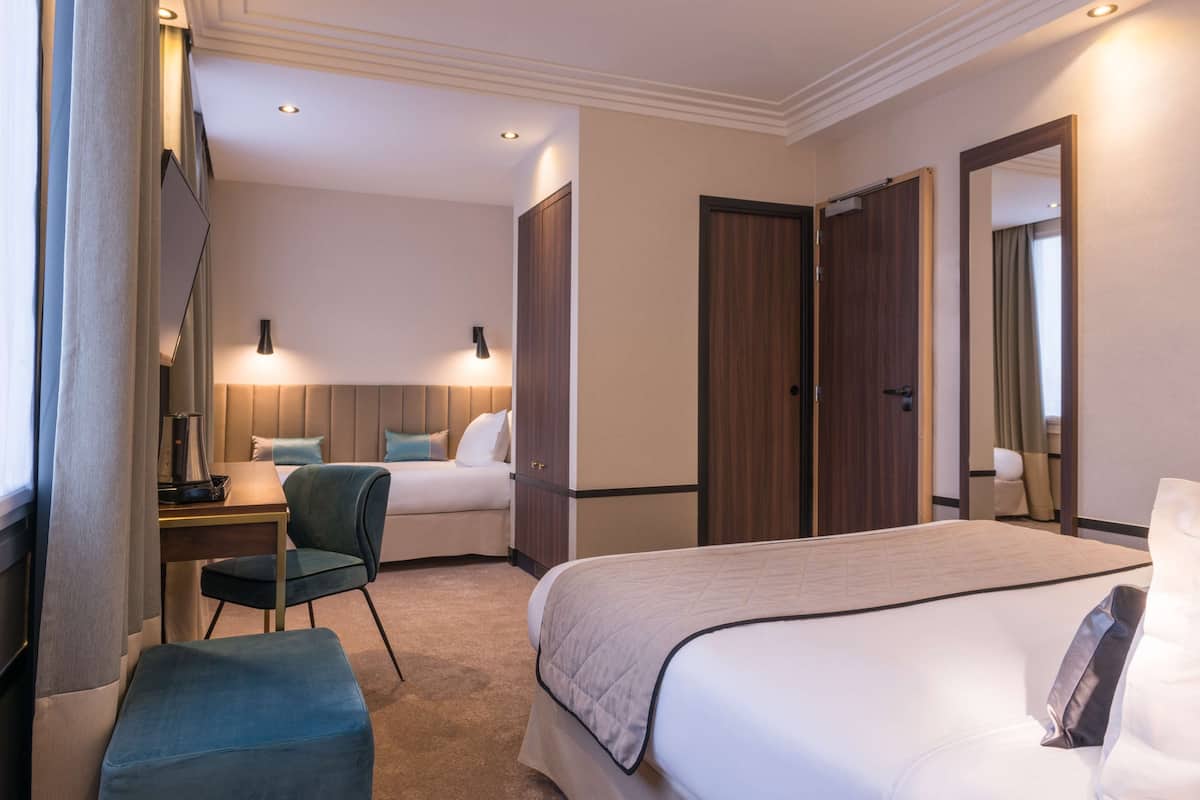 A hotel room with a bed, a desk with a chair, a small table, and a wardrobe.