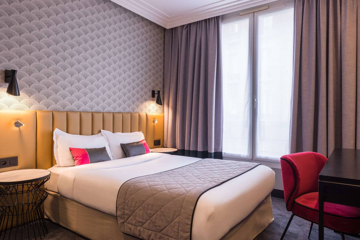 A hotel room with a large bed, a desk, a chair, and a round table.