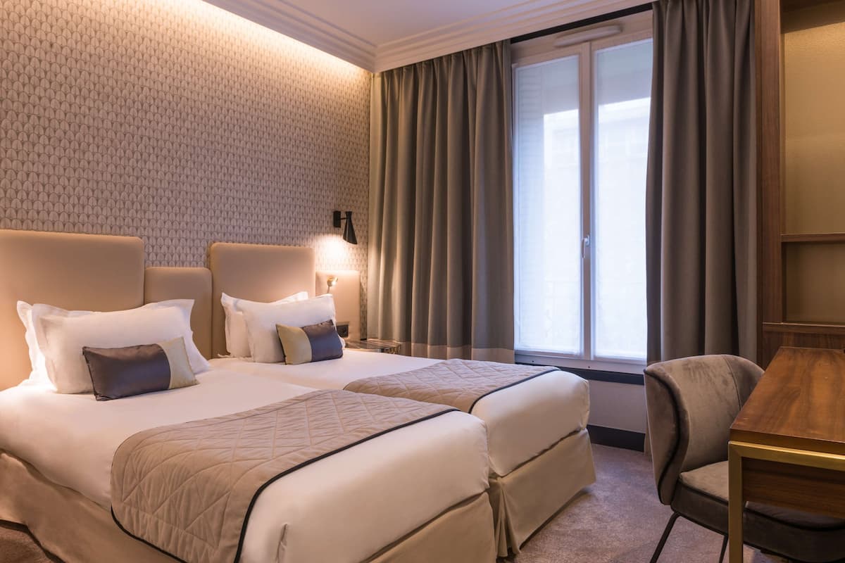 A hotel room with two beds, a desk, a chair, and a large window with curtains.
