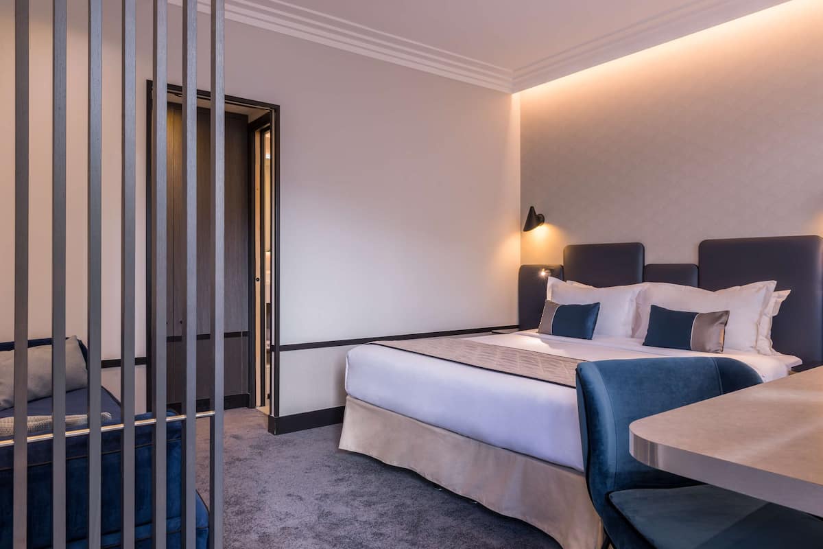 A hotel room with a bed, bedside table, and a seating area with a chair.