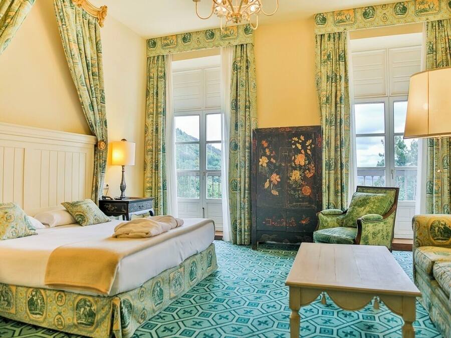A hotel room with a bed, a chair, a table, and a nightstand.