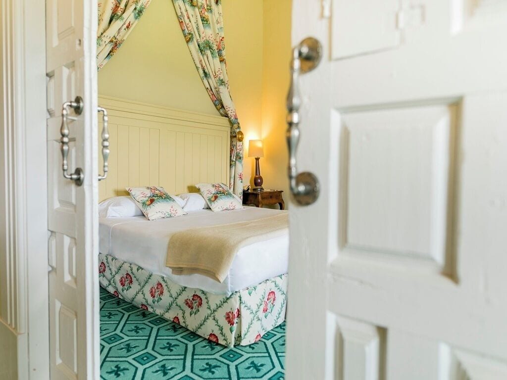 Una stanza con un letto, tende floreali, una lampada da comodino e piastrelle a pavimento decorate.