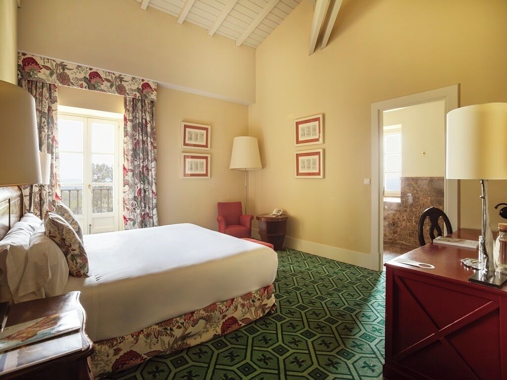 A hotel room with a bed, a desk, a chair, a lamp, and a window with curtains.