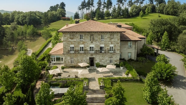 A large stone building with a tiled roof, surrounded by lush greenery and a well-maintained lawn. - Palacio Urgoiti (Mungia)