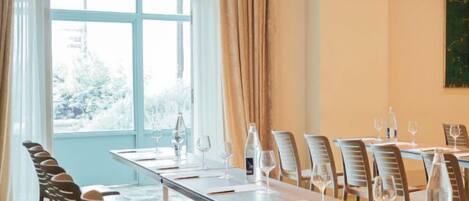 A conference room with a long table, chairs, and a large window with curtains.
