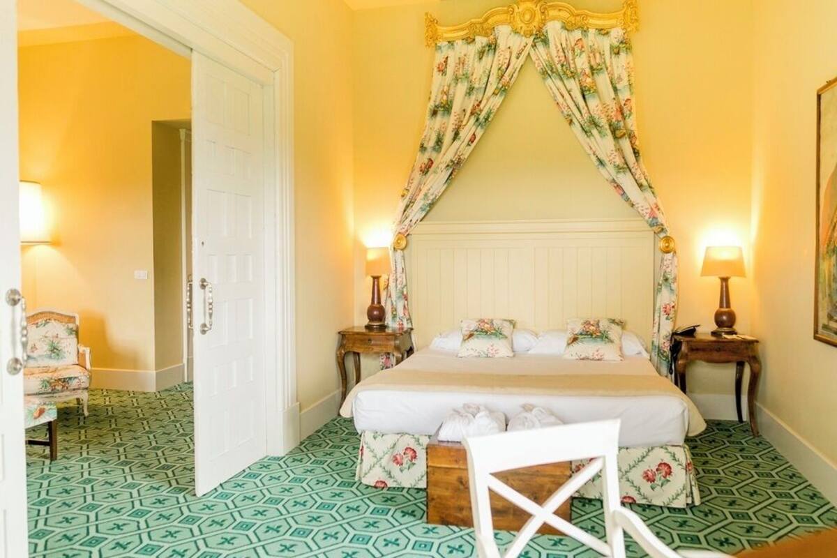 Una habitación de hotel con cama, cortinas florales, piso estampado y una silla.